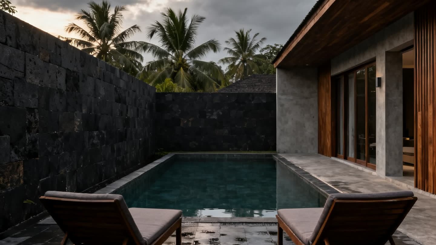 An unoccupied pool villa terrace with empty loungers and still water under overcast skies, on a tropical island in the low season.